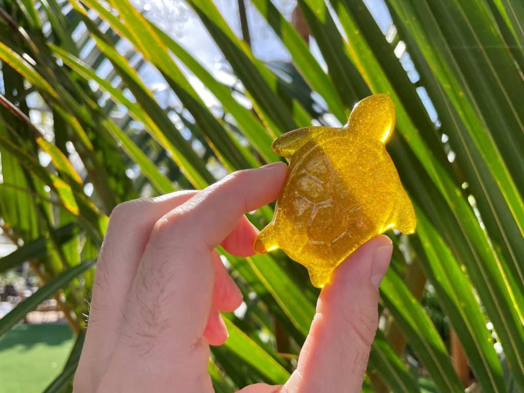 A gold-colored glass sea turtle found in front of a palm tree